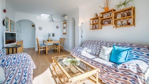 A living room with a sofa, a coffee table, a dining table with chairs, and a TV. - Apartment Carabela 44 on Alcudia Beach (Alcúdia)