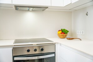 Een keuken met een fornuis, oven en een kom fruit op het aanrecht.