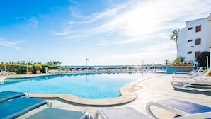 A pool area with lounge chairs and a building in the background. - Apartment Carabela 44 on Alcudia Beach (Alcúdia)