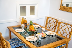 Et spisebord med glasplade, omgivet af fletstole, dækket med tallerkener, bestik og en ananas som midtpunkt.