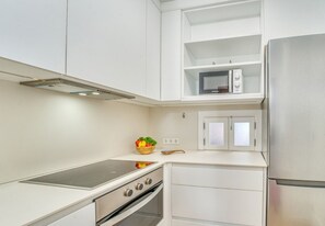 A compact kitchen with white cabinetry, a built-in microwave, a stainless steel refrigerator, a gas stove, and an oven.