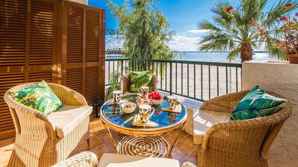 A balcony with wicker furniture, a glass table, and a view of the sea. - Apartment Carabela 44 on Alcudia Beach (Alcúdia)