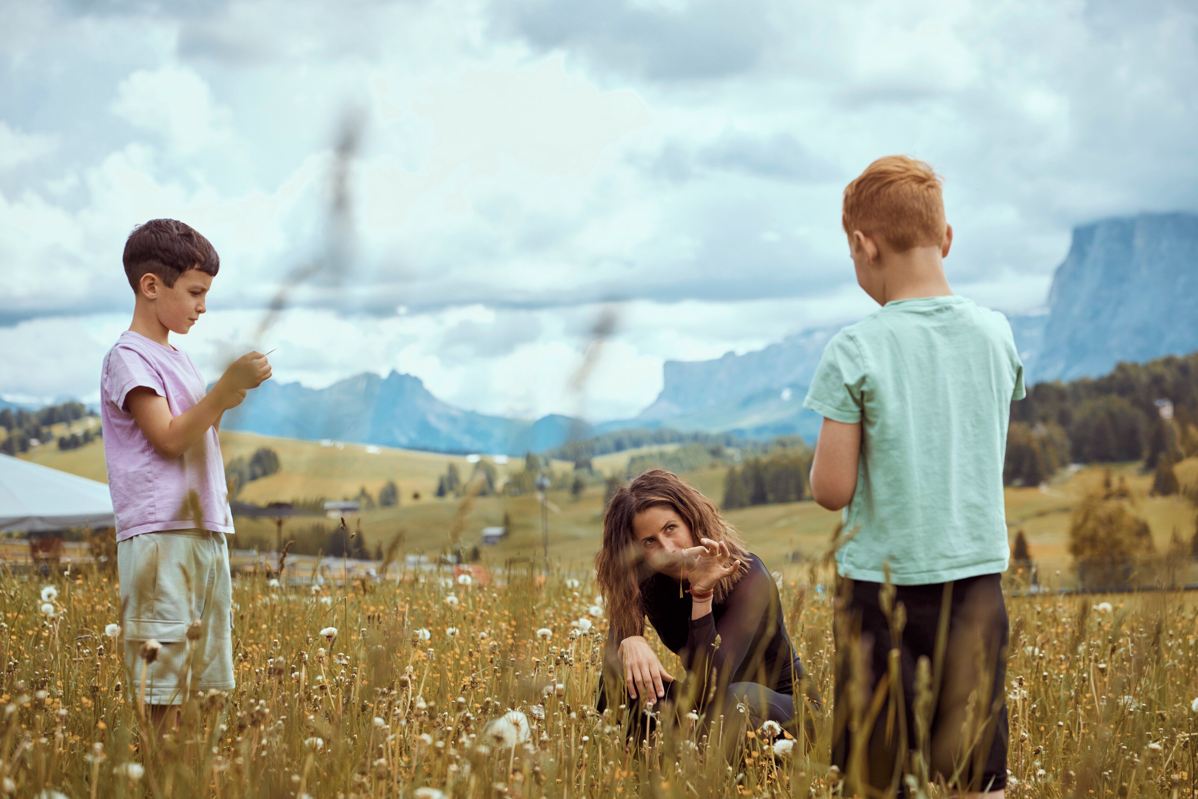 Three children in a field with mountains in the background.