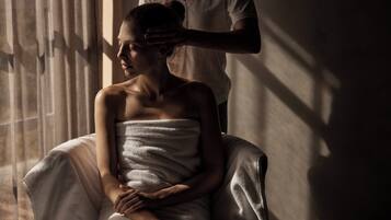 A person seated in a room with a window, a curtain, and a wall.