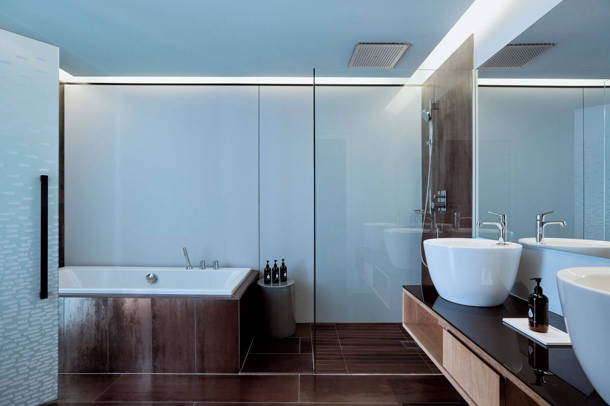A modern bathroom with a large bathtub, two sinks, and a glass shower enclosure.