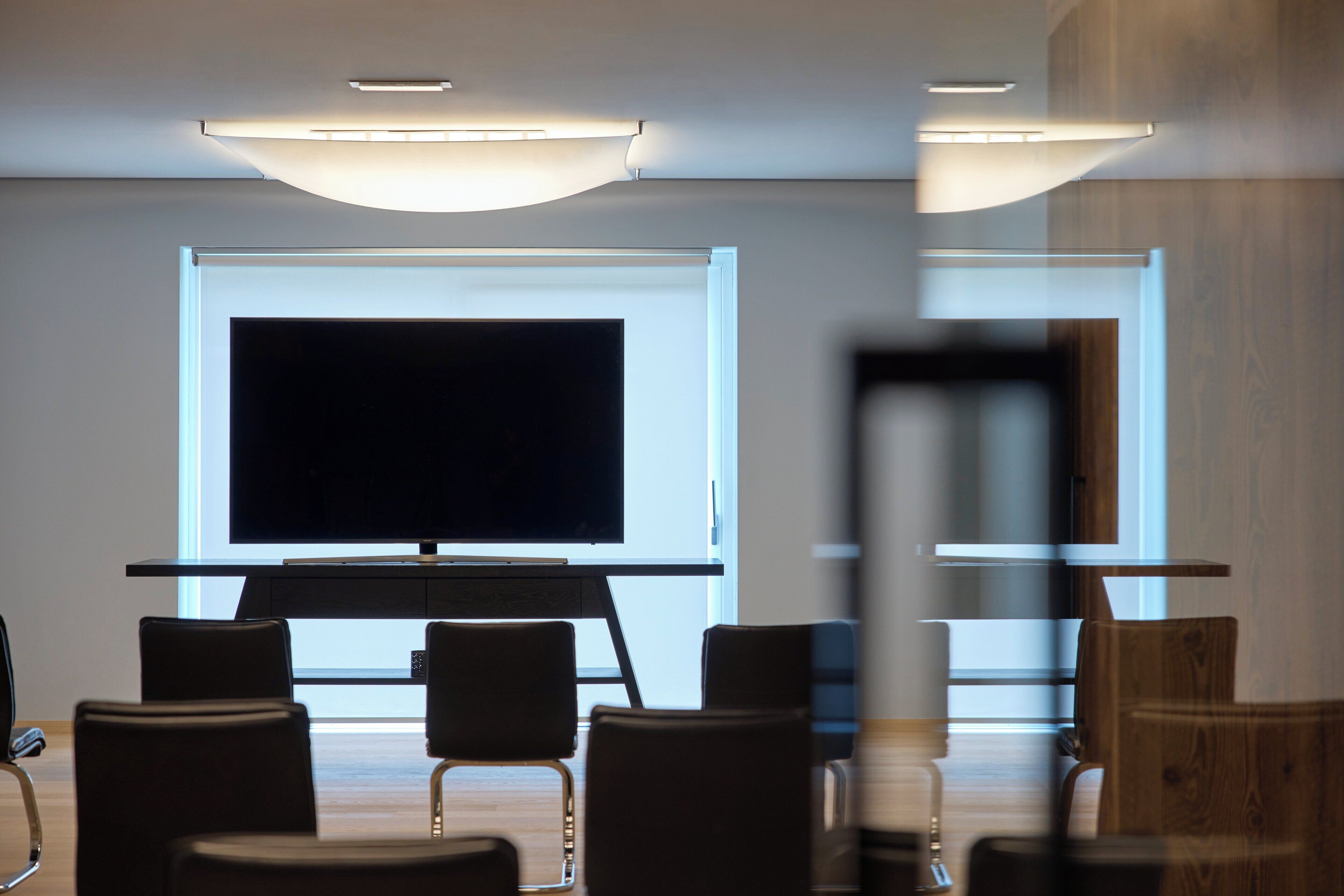 A conference room with a large flat-screen TV, modern chairs, and a wooden accent wall.