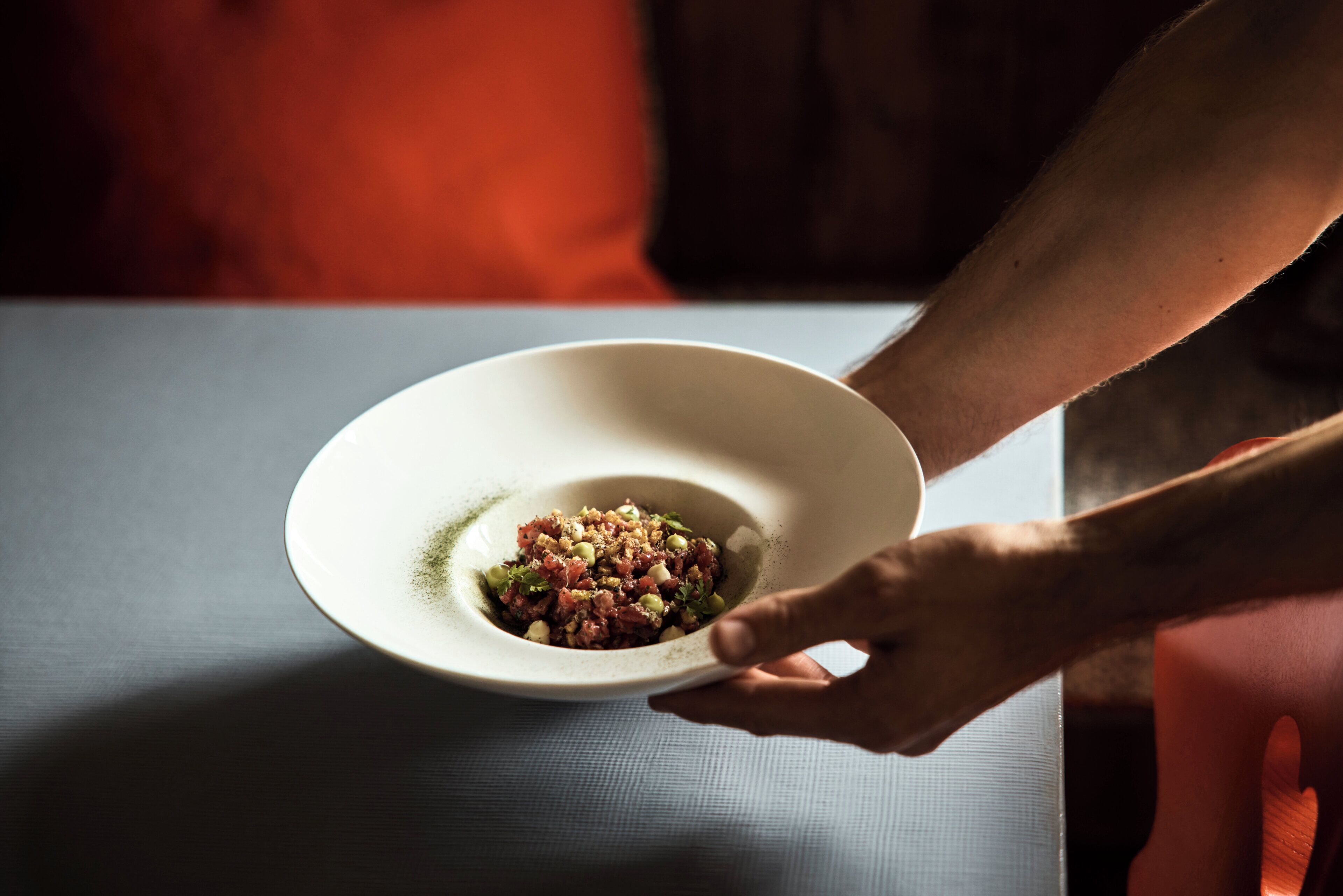 A hand holding a bowl of food on a table.