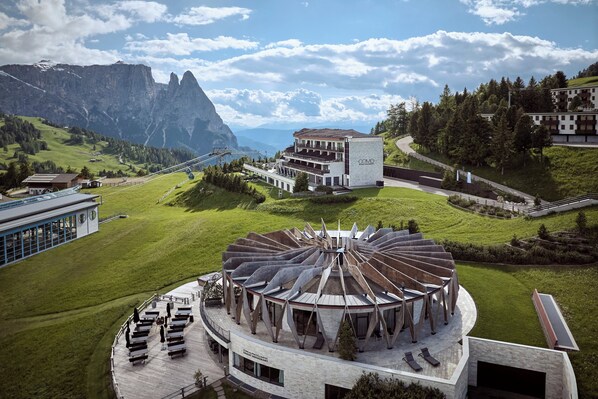A modern hotel with a circular central structure, a mountain backdrop, and a clear sky.