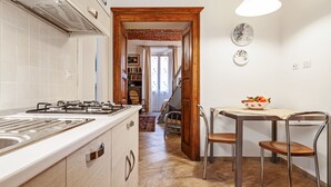 A kitchen with a gas stove, wooden cabinets, and a dining area with two chairs and a table. - Acqui Terme - Via Manzoni 5 (Acqui Terme)