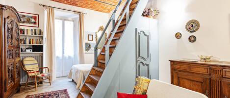 Una sala de estar con una escalera, un sofá, un armario de madera y una estantería.