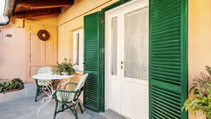 A patio with a table and chairs, a door with green shutters, and a wreath on the wall. - Acqui Terme - Via Manzoni 5 (Acqui Terme)