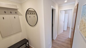 Een gang met een bank, kapstok, spiegel en een deur naar een andere kamer.