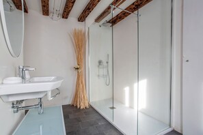 A modern bathroom with a glass shower enclosure, a white sink with chrome fixtures, and a mirror above the sink.