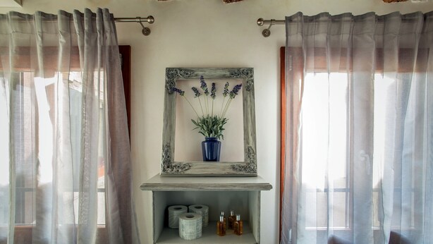 A bathroom with a rustic mirror, a shelf with toiletries, and sheer curtains. - Venezia - Calle Furlani 3277 (Venice)