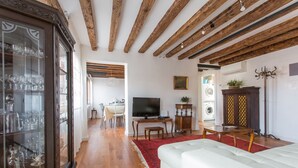 A living room with wooden beams, a white sofa, a TV, and a cabinet with glass doors. - Venezia - Calle Furlani 3277 (Venice)