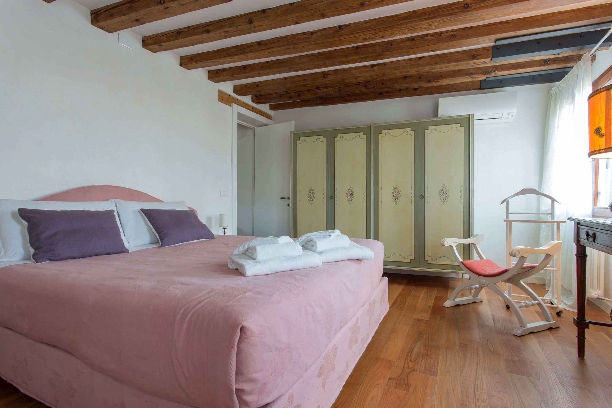 A bedroom with a bed, a wardrobe, a chair, and a desk with a lamp.