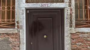 A brown door with a brass handle, flanked by two windows with decorative iron bars. - Venezia - Calle Furlani 3277 (Venice)