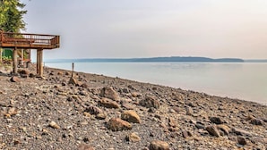 Ein felsiger Strand mit einer Holzkonstruktion, möglicherweise einer Aussichtsplattform, mit Blick auf ruhiges Wasser und ferne Hügel.