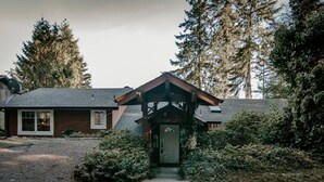 Ein Holzhaus mit Veranda, umgeben von dichten Bäumen und einer Schotterzufahrt.