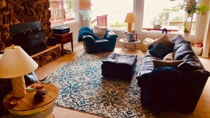 Ein Wohnzimmer mit Steinwand, Kamin, blauem Sessel, schwarzem Sofa und einem gemusterten Teppich.