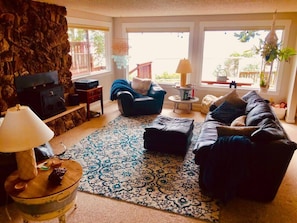 A living room with a stone wall, a fireplace, a blue armchair, a black sofa, and a patterned rug.