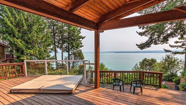 Eine Holzterrasse mit einer Matratze, Stühlen und Blick auf das Meer.