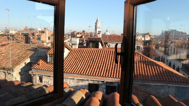 A view from a window overlooking a cityscape with terracotta-tiled rooftops and a prominent white tower. - Venezia - Calle De Le Vele (Venice)