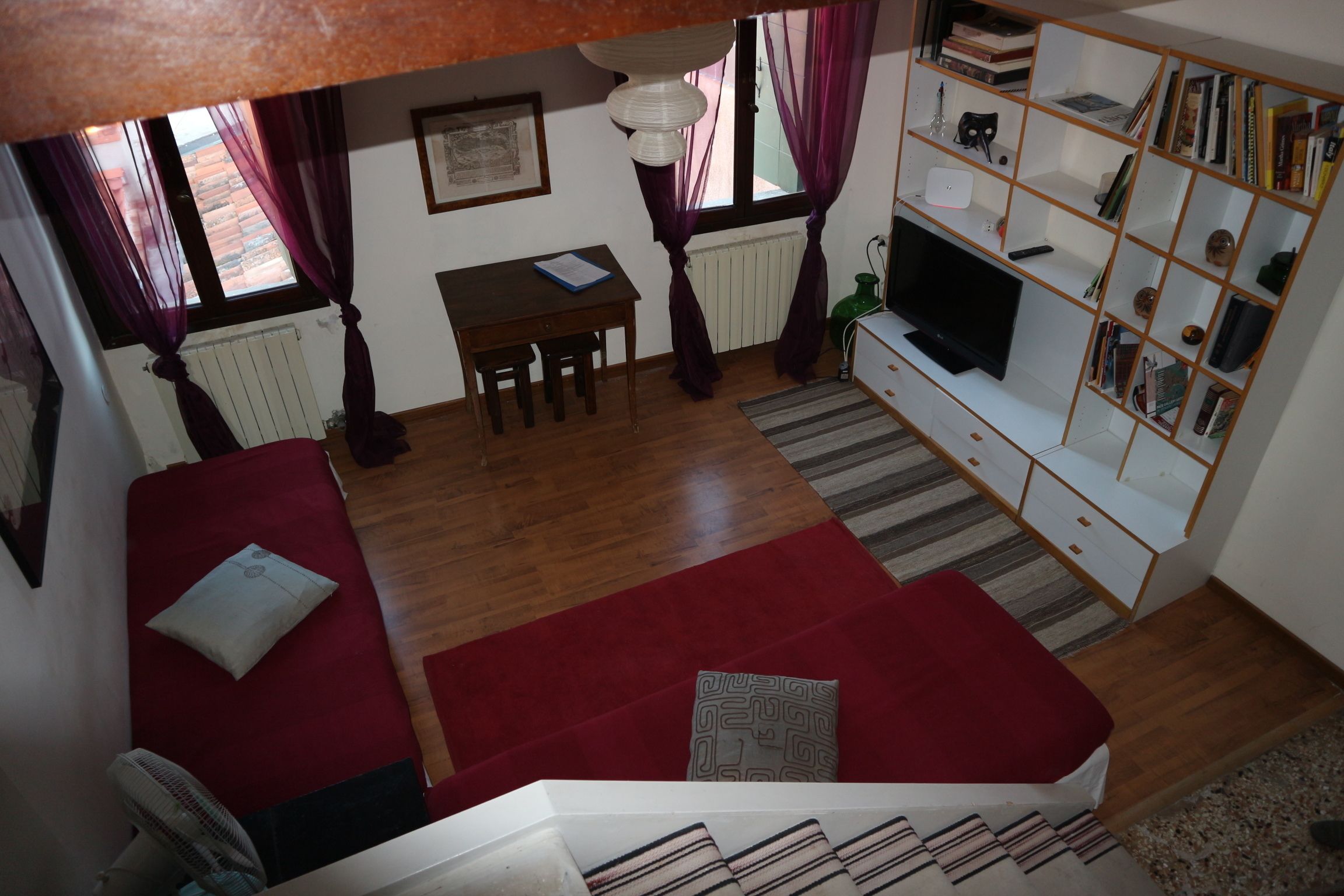 Una sala de estar acogedora con un sofá rojo, una mesita, un televisor y una estantería.
