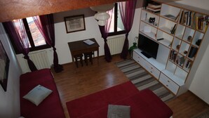 A cozy living room with a red sofa, a small table, a TV, and a bookshelf. - Venezia - Calle De Le Vele (Venice)