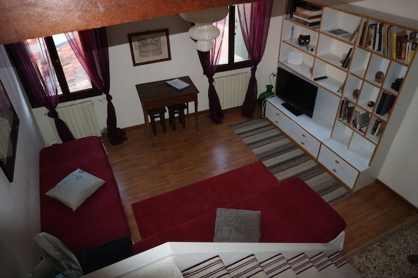 Una sala de estar acogedora con un sofá rojo, una mesita, un televisor y una estantería.