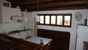 A compact kitchen with wooden cabinets, a white countertop, and a dining area with a wooden table and chairs. - Venezia - Calle De Le Vele (Venice)