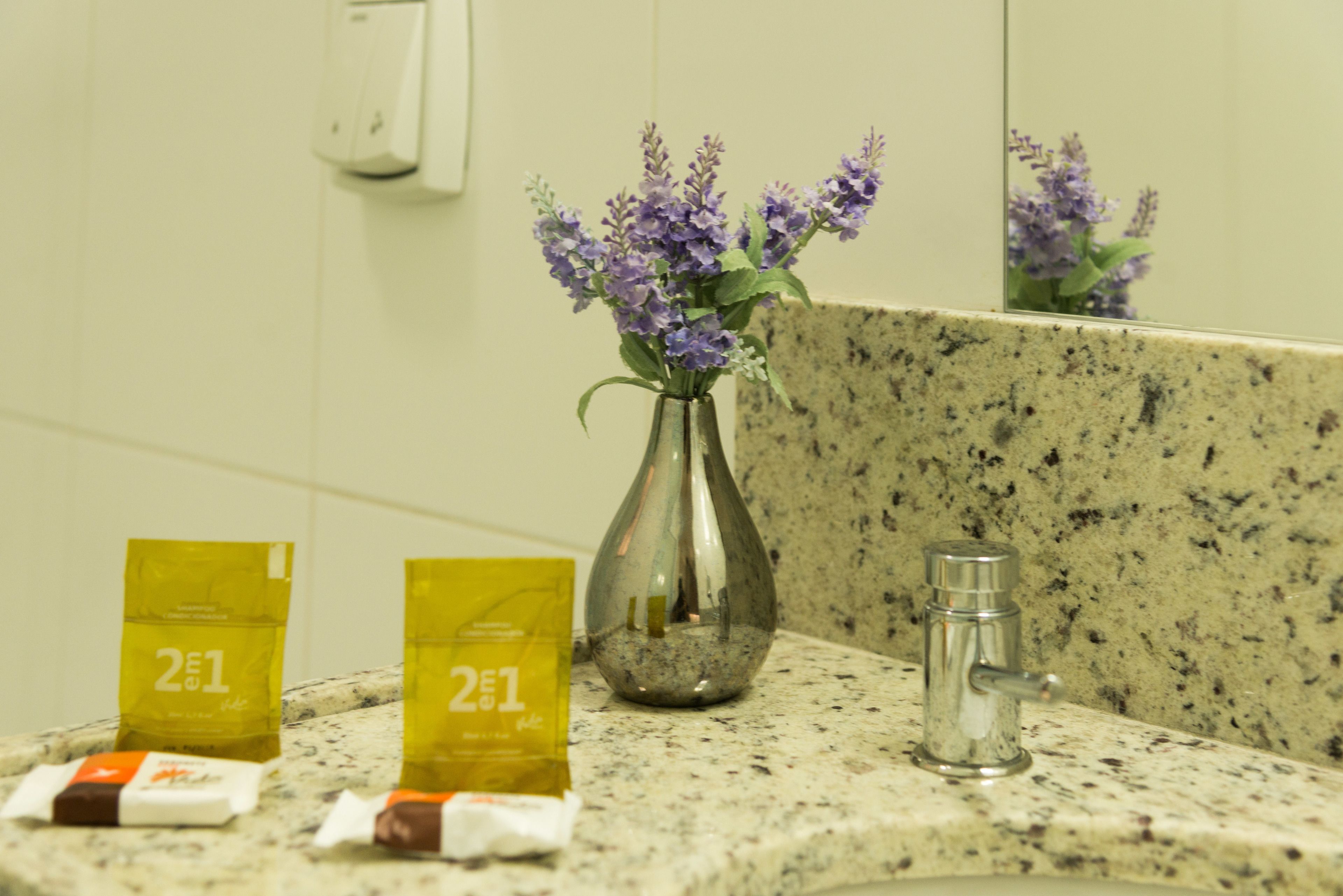 A bathroom with a granite countertop, a vase with purple flowers, and two yellow packets labeled "2E1".