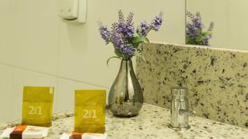 A bathroom with a granite countertop, a vase with purple flowers, and two yellow packets labeled "2E1".