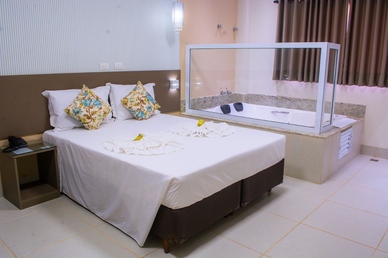 A hotel room with a bed, a bedside table with a phone, a glass-enclosed bathtub, and a small vanity area.