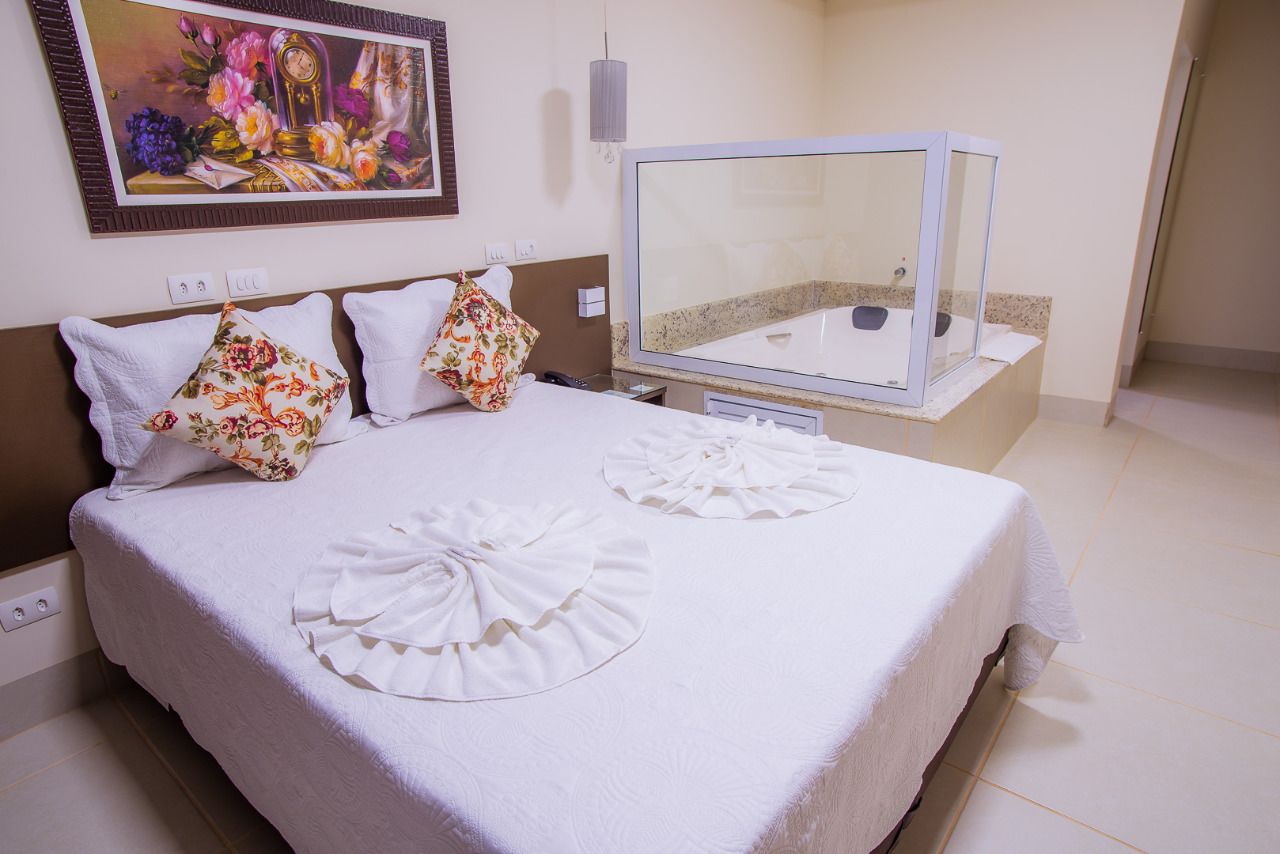 Quarto de hotel com cama, um espelho grande, um quadro na parede e uma mesinha com telefone e abajur.