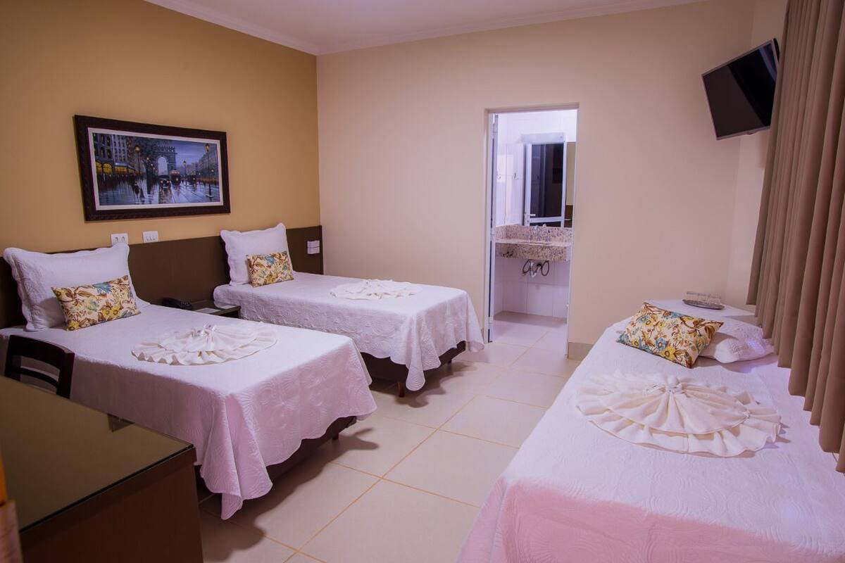 Una habitación de hotel con dos camas, un escritorio, una silla, un televisor y un cuadro en la pared.