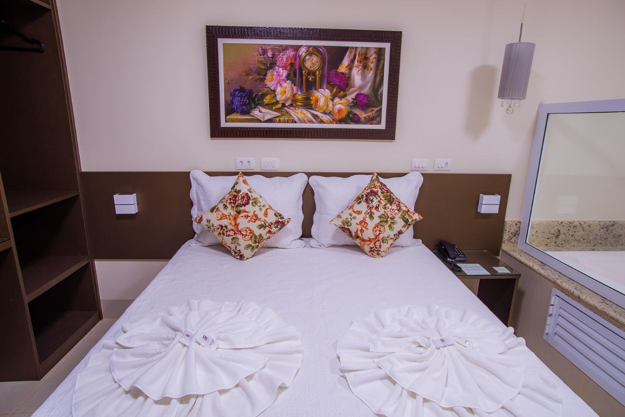 Habitación de hotel con una cama, almohadones estampados, un cuadro sobre la cama, una mesita de noche y un armario.