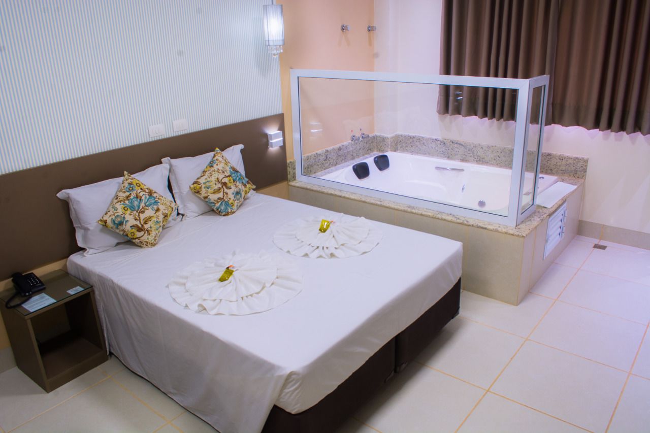 A hotel room with a bed, a glass-enclosed jacuzzi, a bedside table with a phone, and a nightstand.