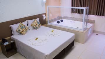 A hotel room with a bed, a glass-enclosed jacuzzi, a bedside table with a phone, and a nightstand.