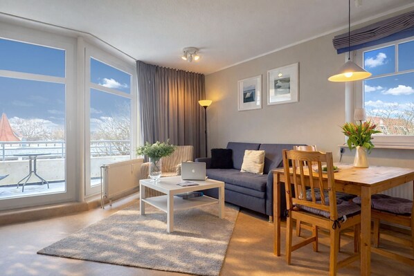 A modern living room with a sofa, coffee table, dining table, and chairs. There are large windows with a view of a snowy landscape.