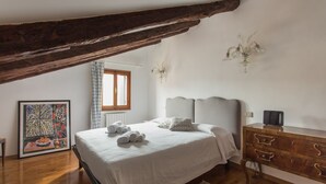 Un dormitorio con cama, tocador, candelabro y ventana con cortinas.