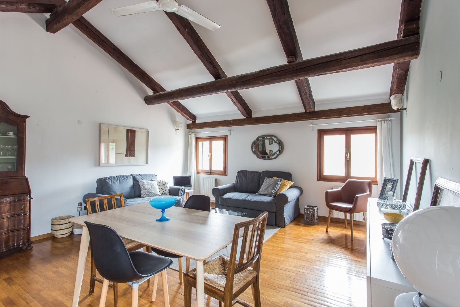 Un vaste espace de vie comprenant une table à manger en bois, deux canapés et un ventilateur de plafond.