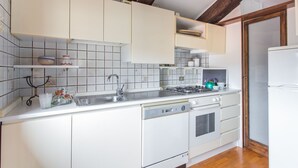 Una cocina con gabinetes blancos, estufa a gas, un lavamanos y refrigerador.