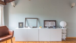 Una sala de estar moderna con piso de madera, un mueble blanco, un sillón de cuero marrón y una lámpara decorativa.