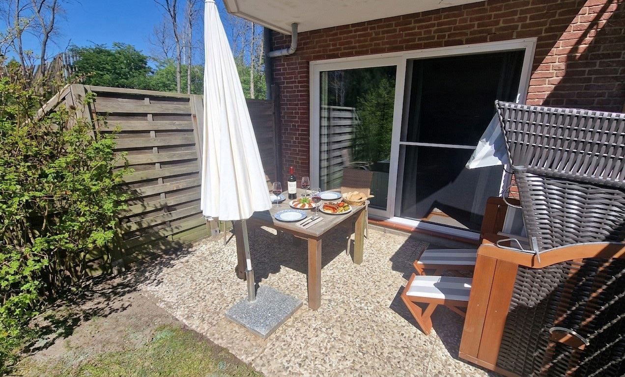 An outdoor patio with a table set for two, a wicker chair, and a covered umbrella.