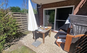 An outdoor patio with a table set for two, a wicker chair, and a covered umbrella.