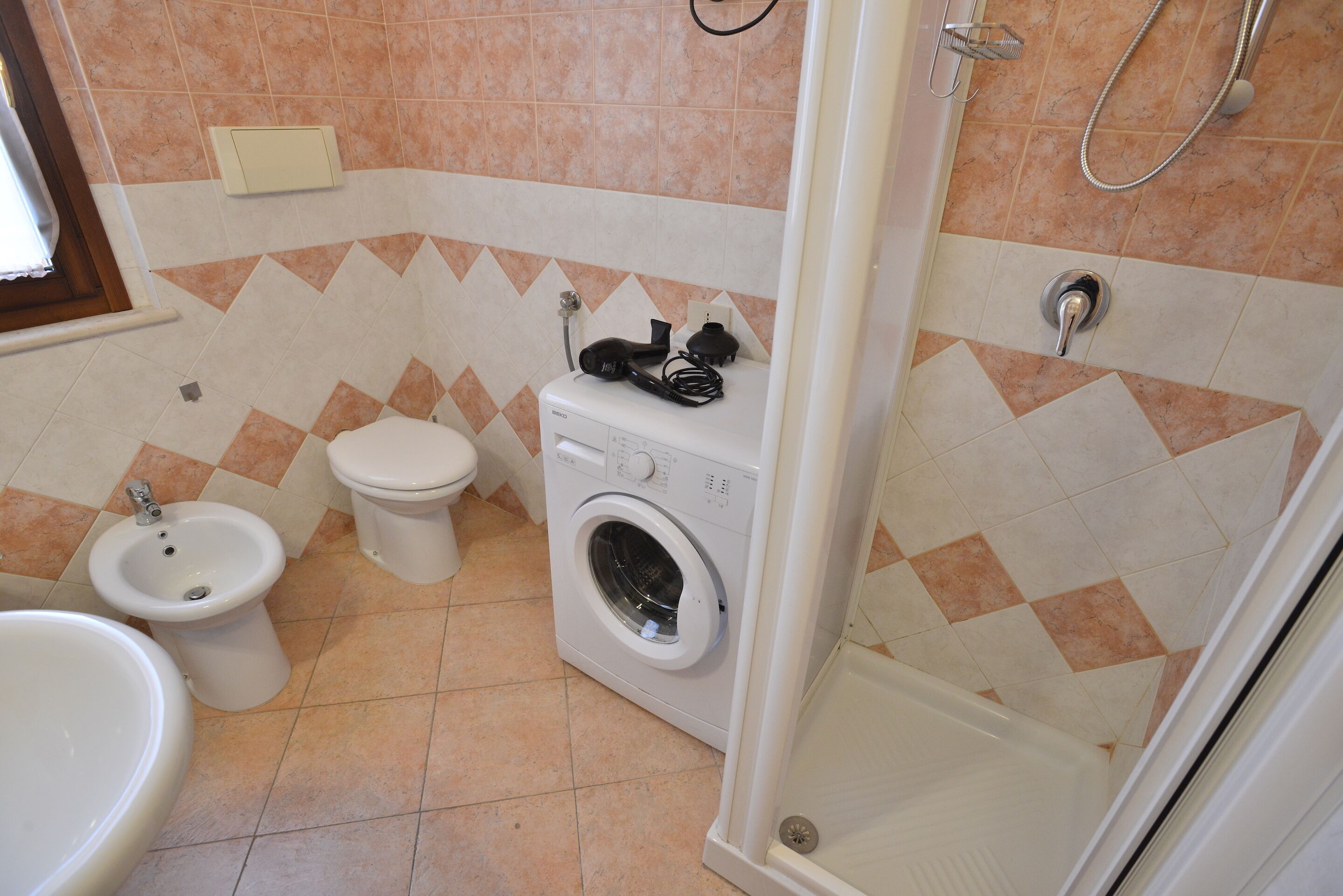 Une salle de bain équipée d’un bidet, de toilettes, d’un lave-linge et d’une douche.