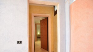 Un pasillo con una puerta de madera, una alfombra de bienvenida y un interruptor de luz en la pared.