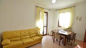 Un sofá amarillo, una mesa de comedor con sillas y una ventana con cortinas.
