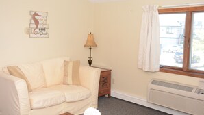 A living room with a beige sofa, a decorative wall piece, a table lamp, a window with curtains, and a wall-mounted heater. - Perfect For Wedding Guest, Friends Getaway Or Family Vacation (Middletown)